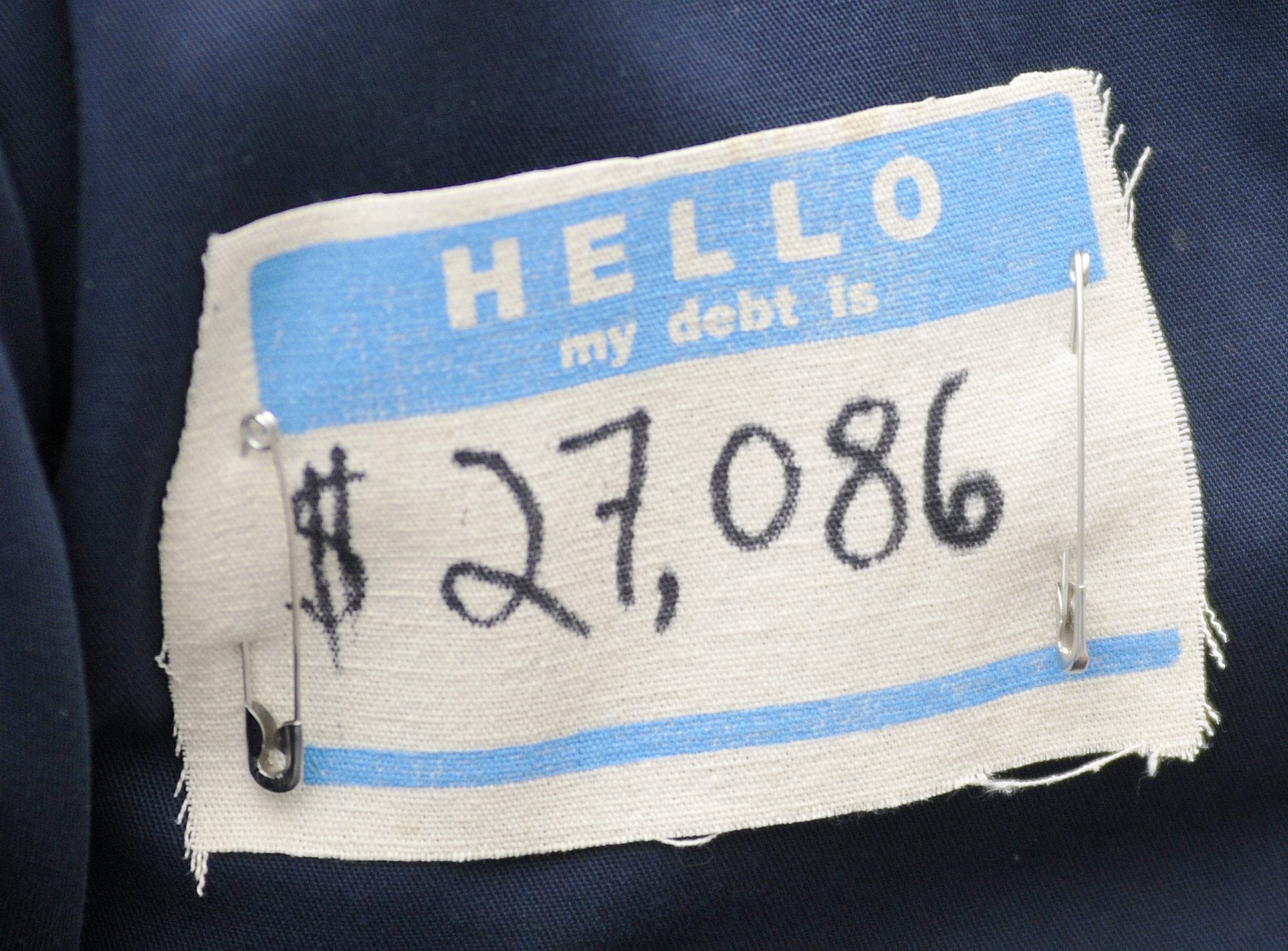 "Hello my debt is ... $27,086" [Picture of a name tag with a person's amount of debt handwritten on it"