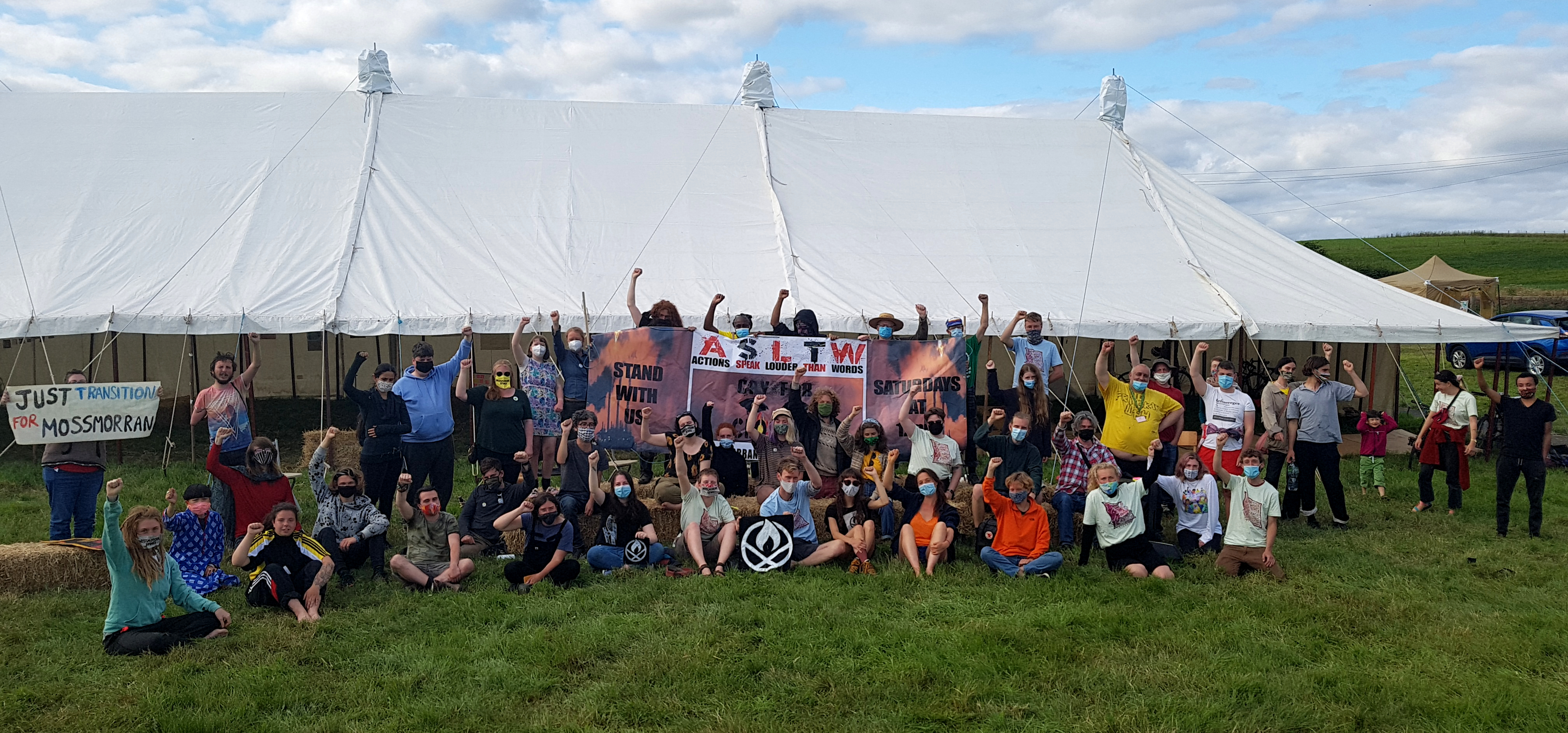 A group of around a dozen climate activists stand in front of a ship called Grampian Sovereign and crates with banners that read CLIMATE JUSTICE = MIGRANT JUSTICE and NO NEW OIL & GAS