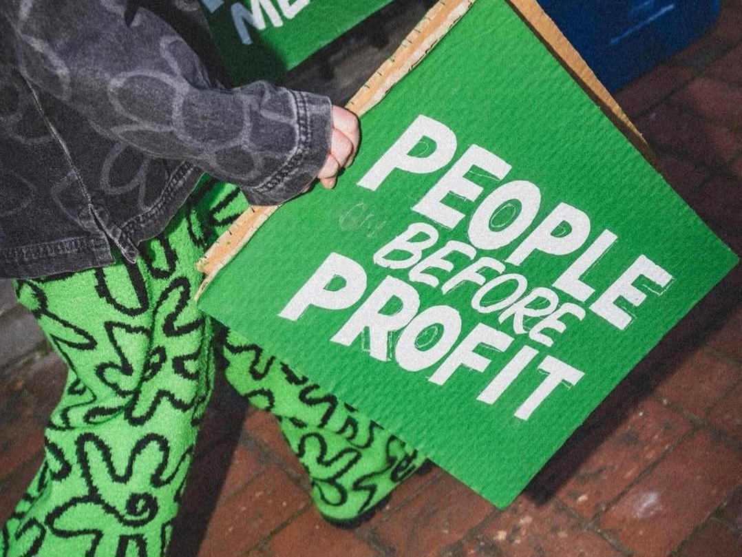 Person walking holding a sign that reads "people before profit"
