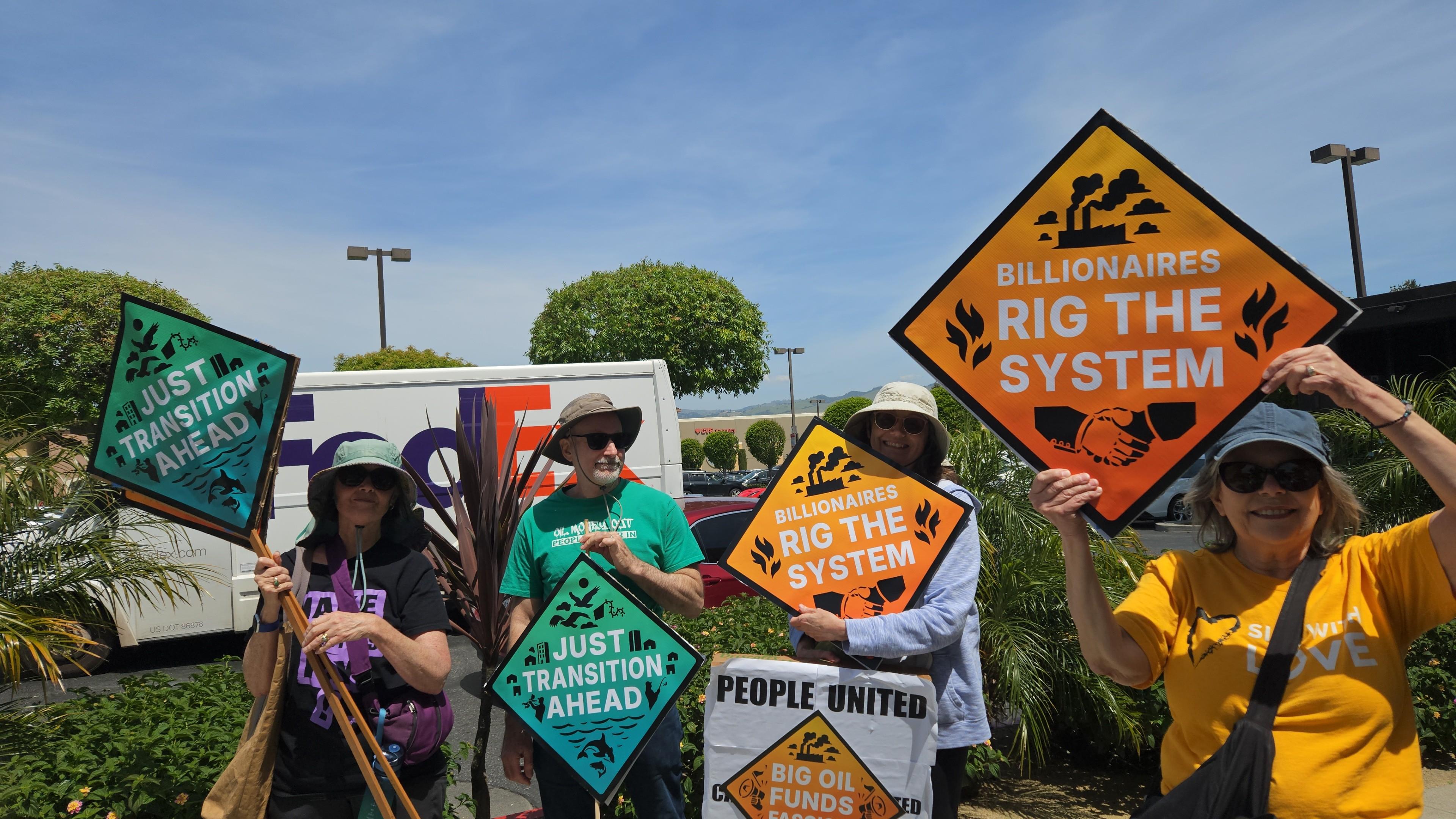 Protesters at a rally in San Jose in May 2026 hold signs that say Just Transition Ahead, Big Oil Funds Fascism and Billionaires Rig the System.