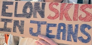 A sign on brown cardboard with block letters in marker, "ELON SKIS IN JEANS"
