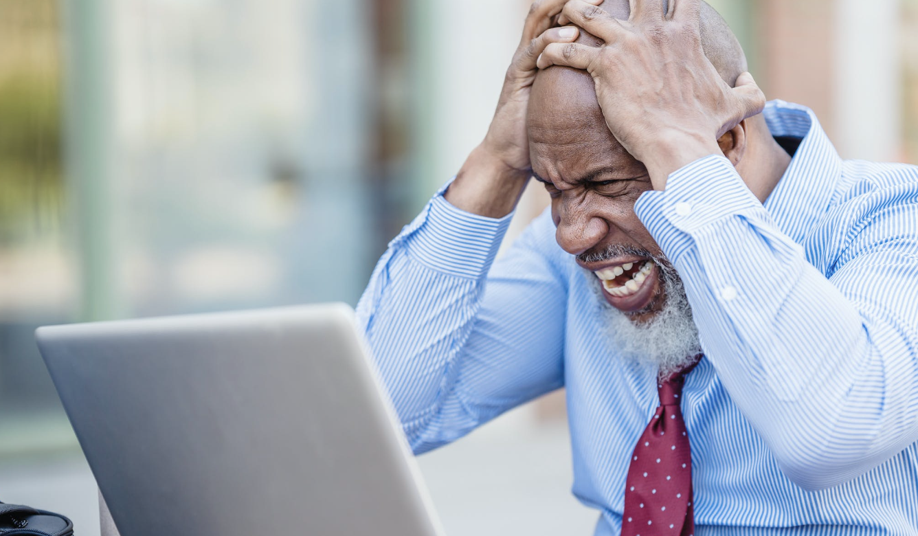 Photograph of a man looking at a laptop in frustration