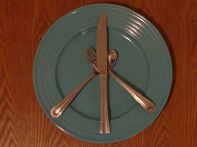 A fork, knife, and spoon on an empty plate make a peace sign