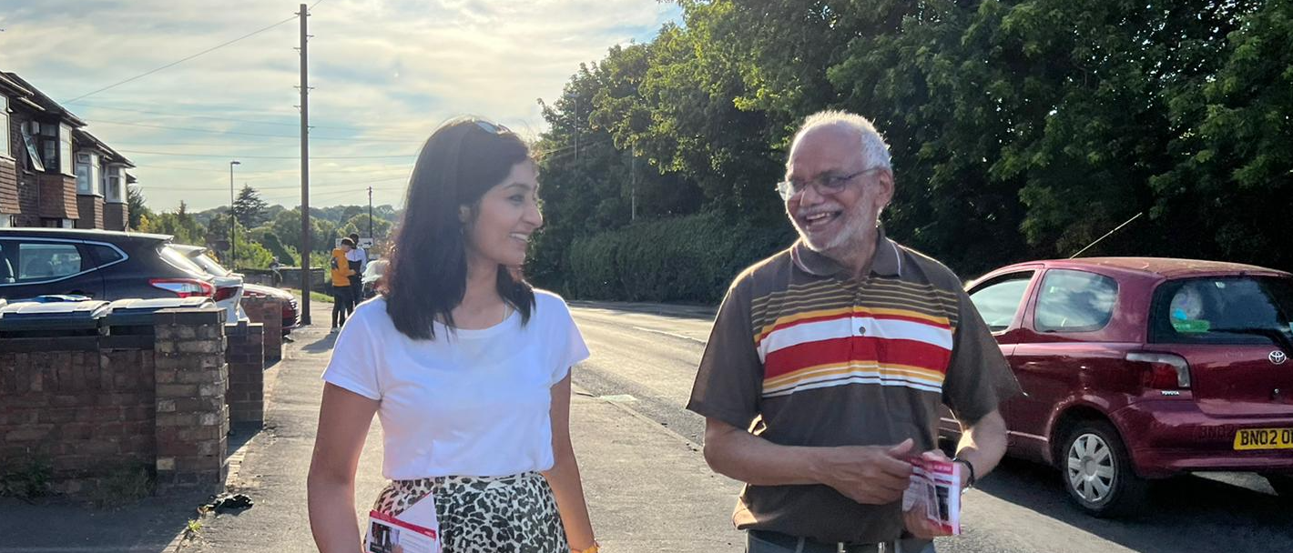 Zarah walking along a road in Coventry with another canvasser. The sun is shining.