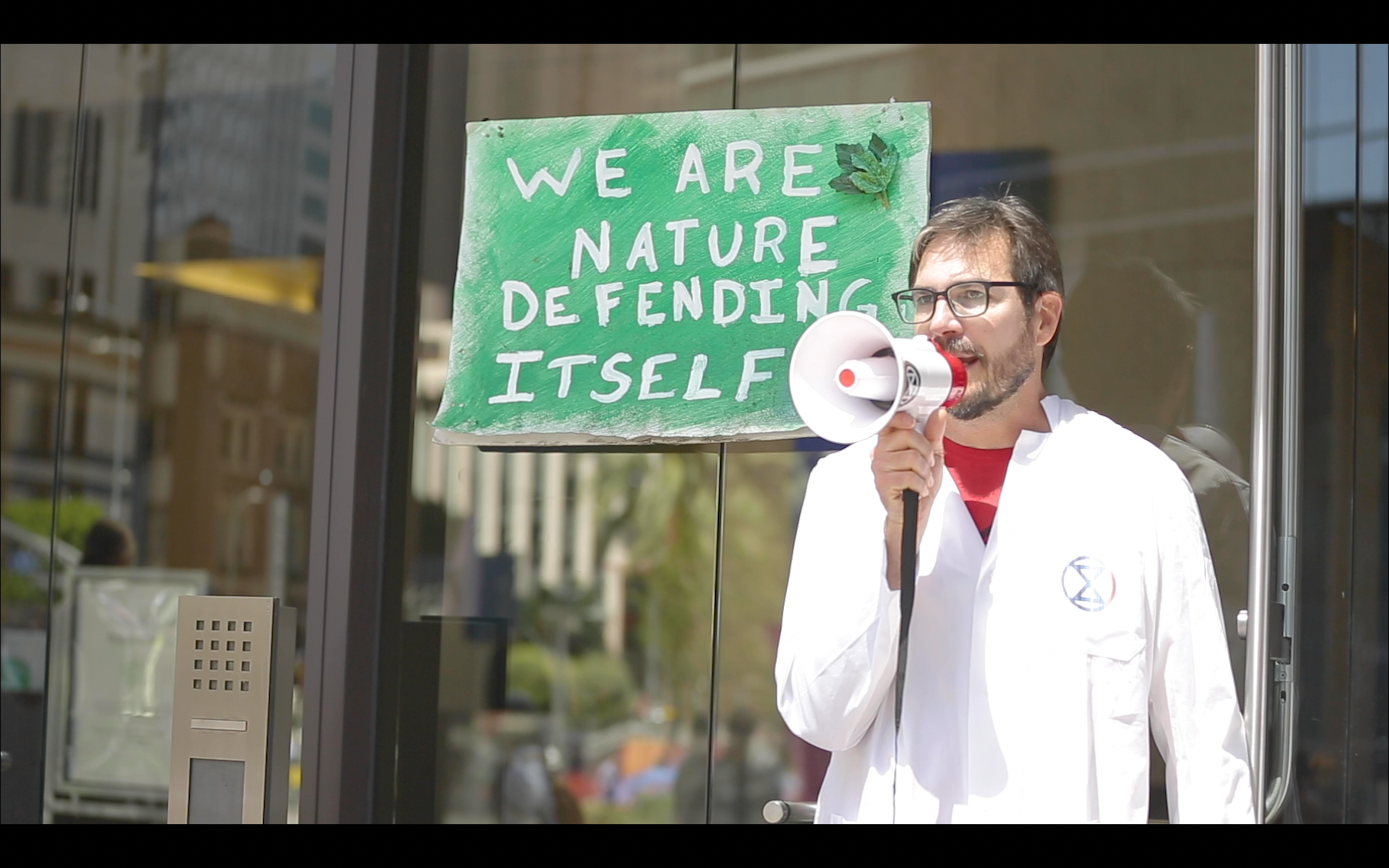 Dr. Peter Kalmus, a NASA scientist, speaking with a megaphone at a climate action. From the film ARRESTING SCIENCE.