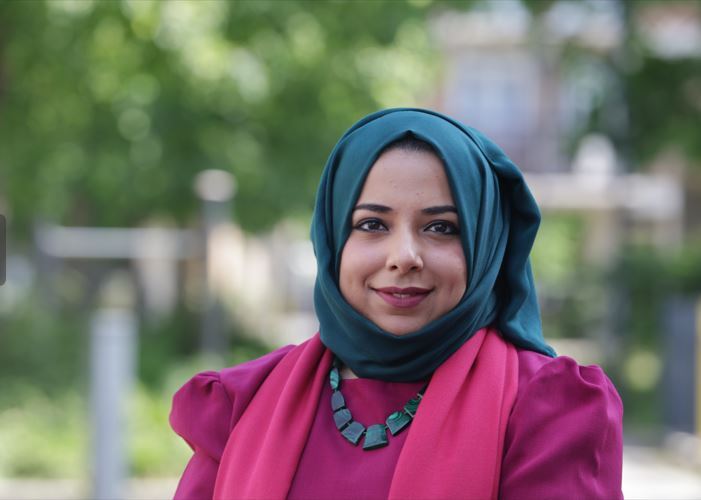 Apsana Begum in a pink dress and green headscarf in front of trees