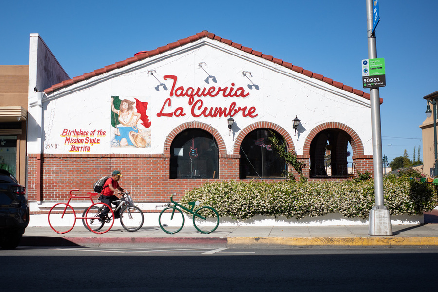 A bicyclist pedals past bike parking racks & a taqueria in San Mateo