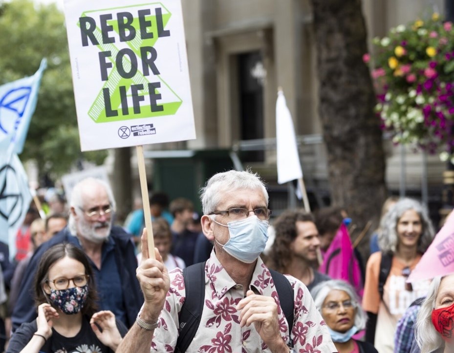 Older people in a protest march. One holds a sign that says 'REBEL FOR LIFE'