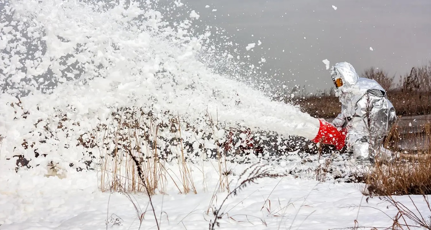 Government employees in hazmat suits spray PFAS containing foam into a prairie stream