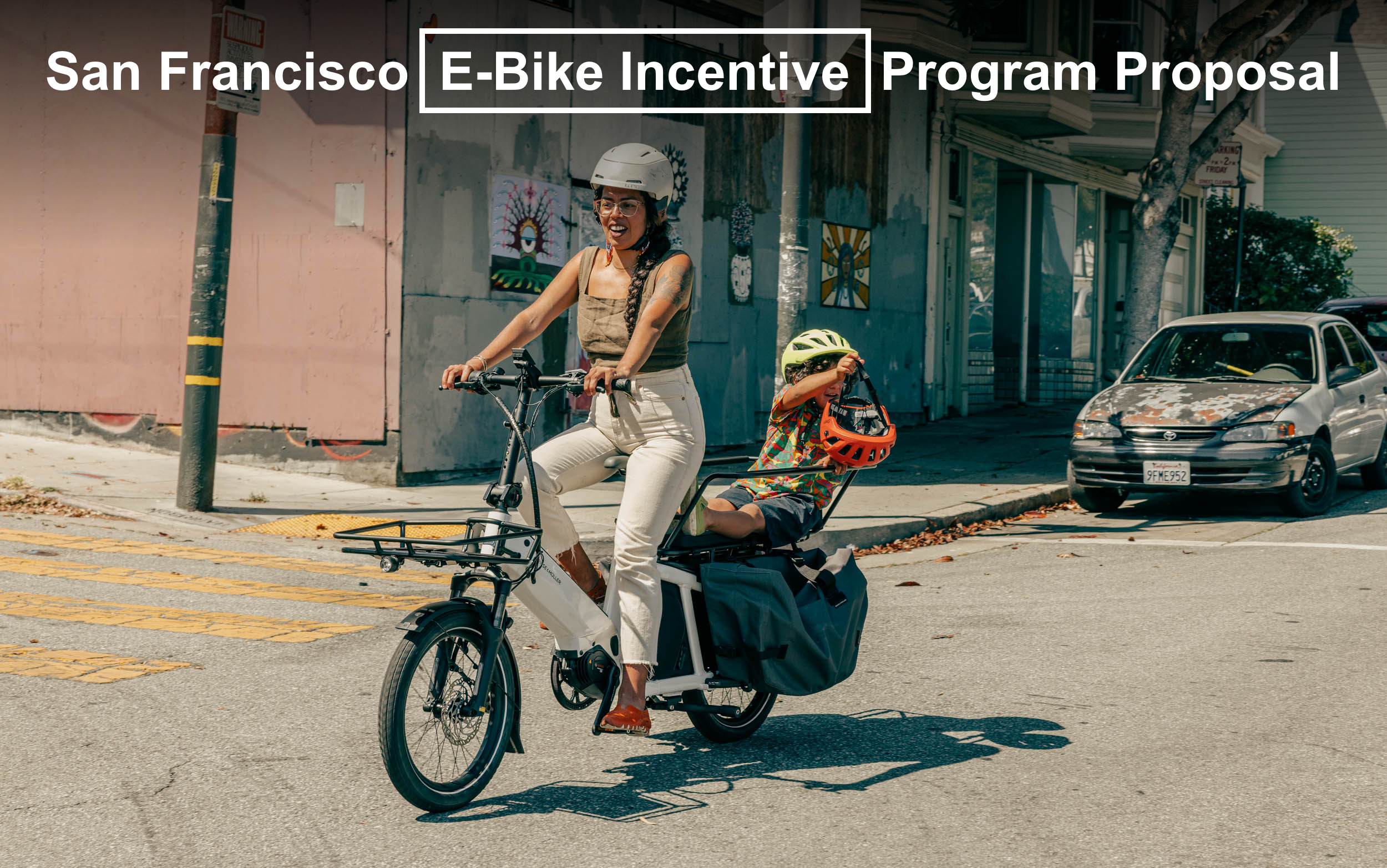 A woman riding an e-bike on a street with a child on the back of the bike who is holding a helmet in their hand