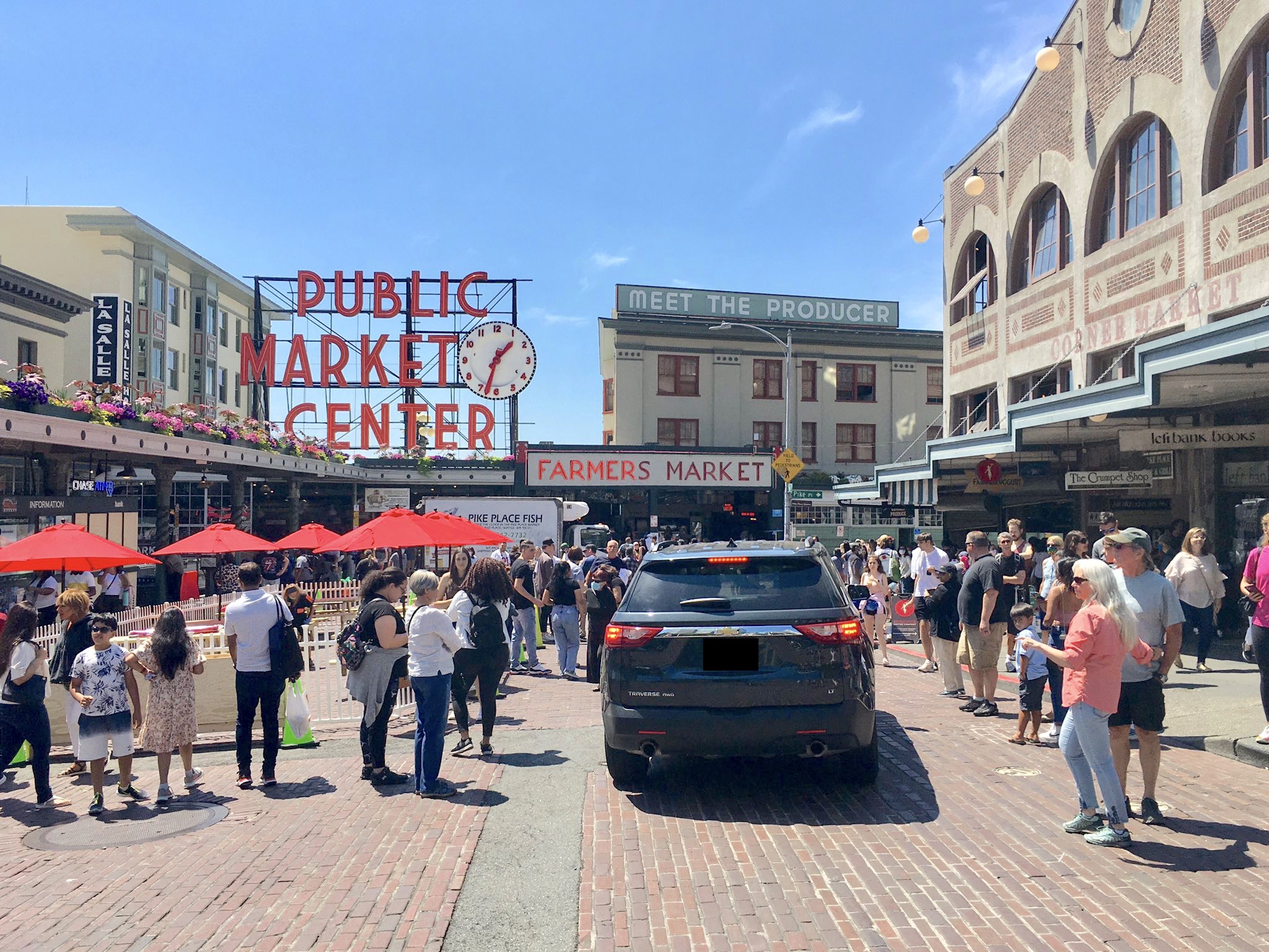 Image of iconic main entrance to Pike Place Market with people walking in the street while a large SUV pushes through the crowd
