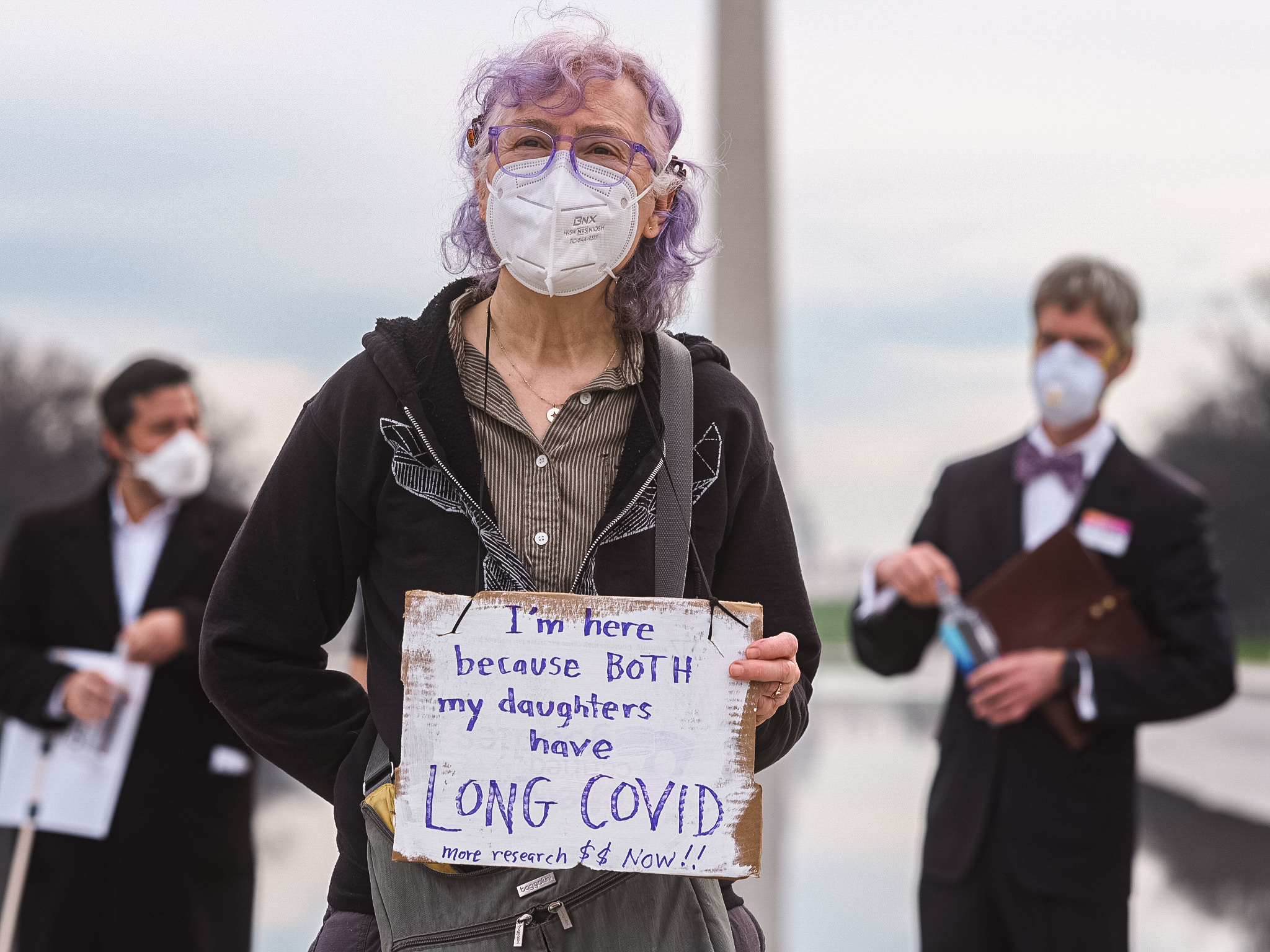 A person holds a sign in front of the Lincoln Memorial during the LCDC demonstration in Washington D.C. on March 15, Long Covid Awareness Day. The sign reads, "I'm here because BOTH of my daughters have Long Covid. More research $$ Now!!" Organizers for the event responded with "“HEAL”, i.e. three Long Covid legislative proposals modeled on bipartisan bills that effectively tackle viral persistence." An action letter is being delivered to Senator Bernie Sanders office calling for HEAL to be adopted into law.