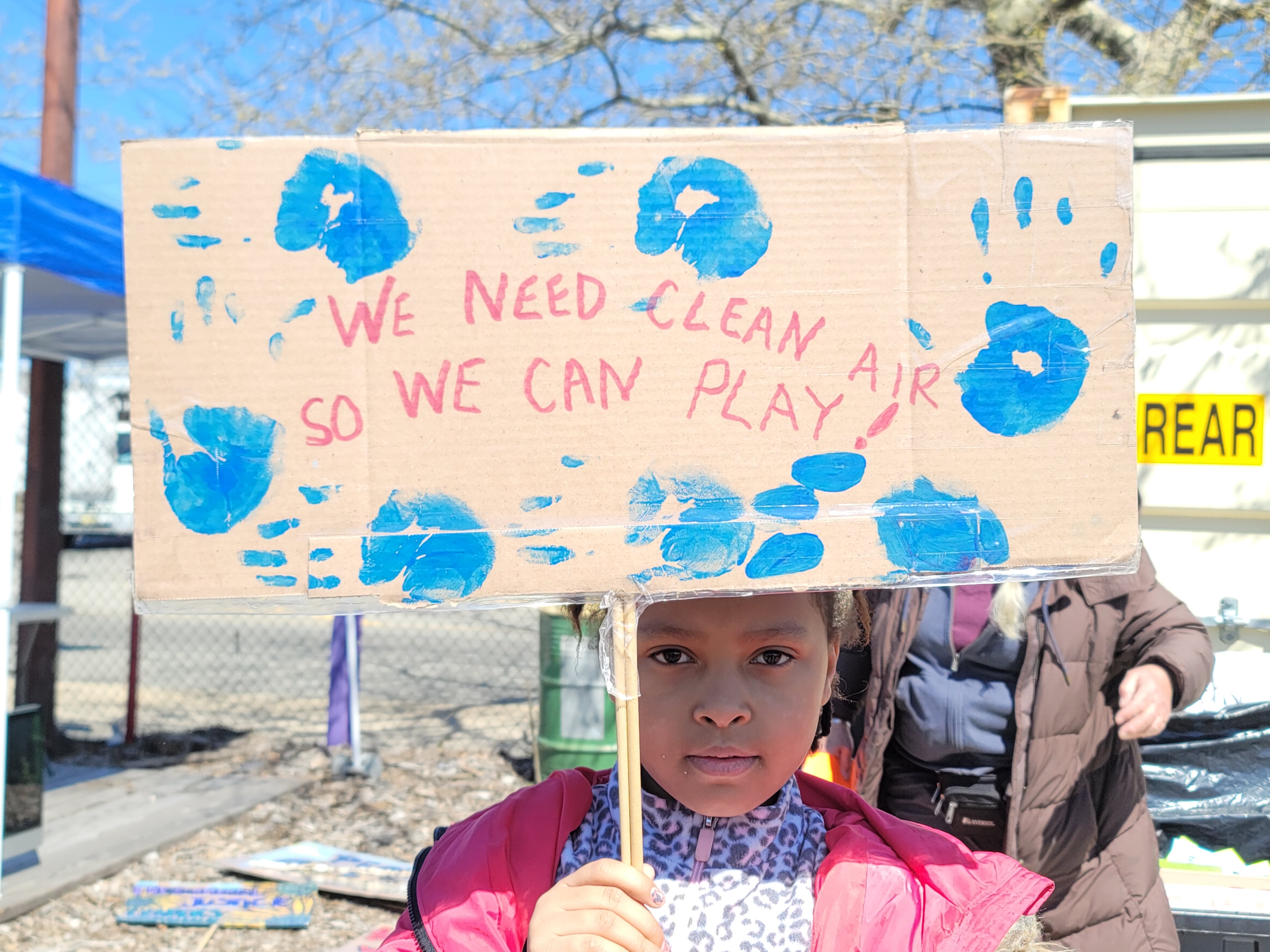 Young advocate for air quality, holding a sign at Down Bottom Farms, location for a press conference highlighting health impacts of cumulative impacts on children and maternal health