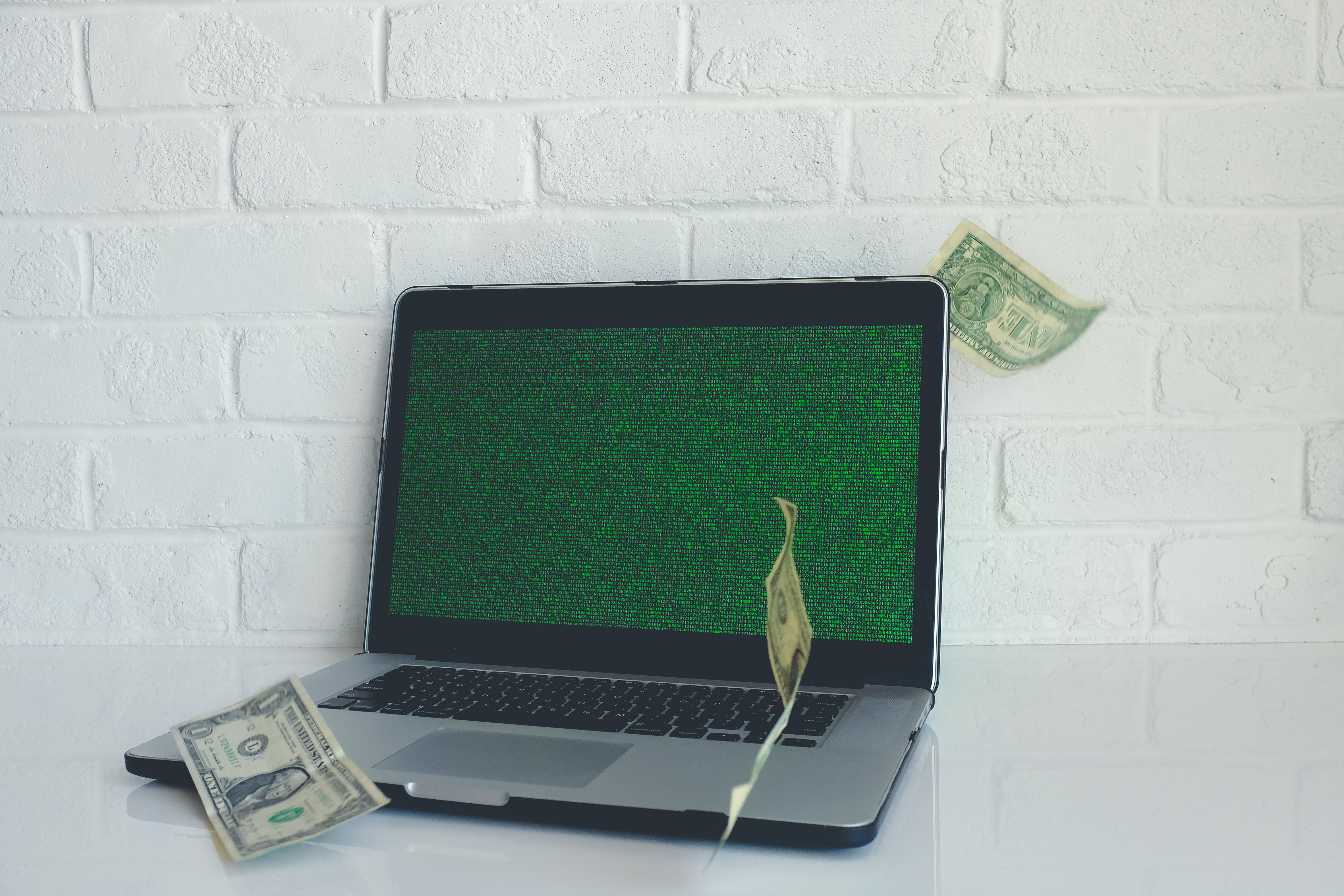 A macbook pro laptop with dollar bills falling on it