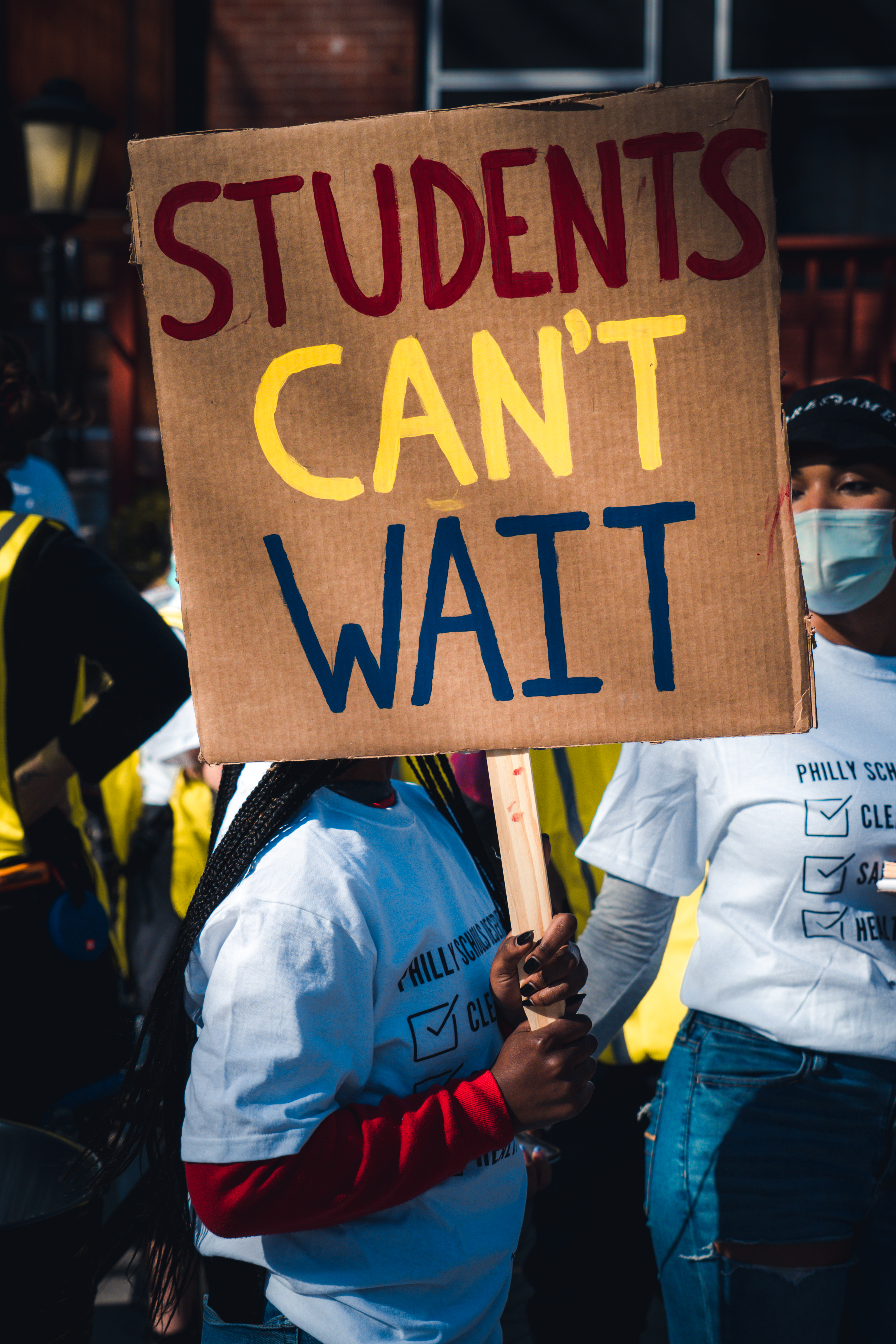 Two organizers hold a large banner painted with the words "Pay PILOTs Now!" #PhillySchoolsDeserve