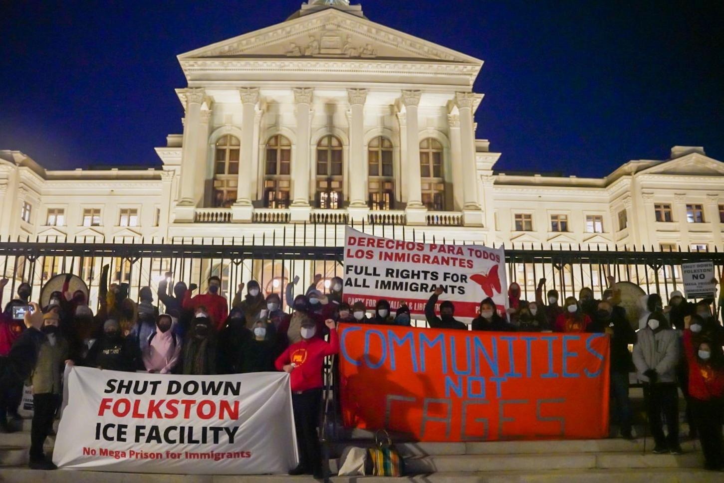 Photo from a protest: a large crowd stands in front of the Georgia Capitol with three banners on display: "Shut Down Folkston ICE Facility," "Communities Not Cages," and "Derechos para todos los inmigrantes! Full rights for all immigrants!"