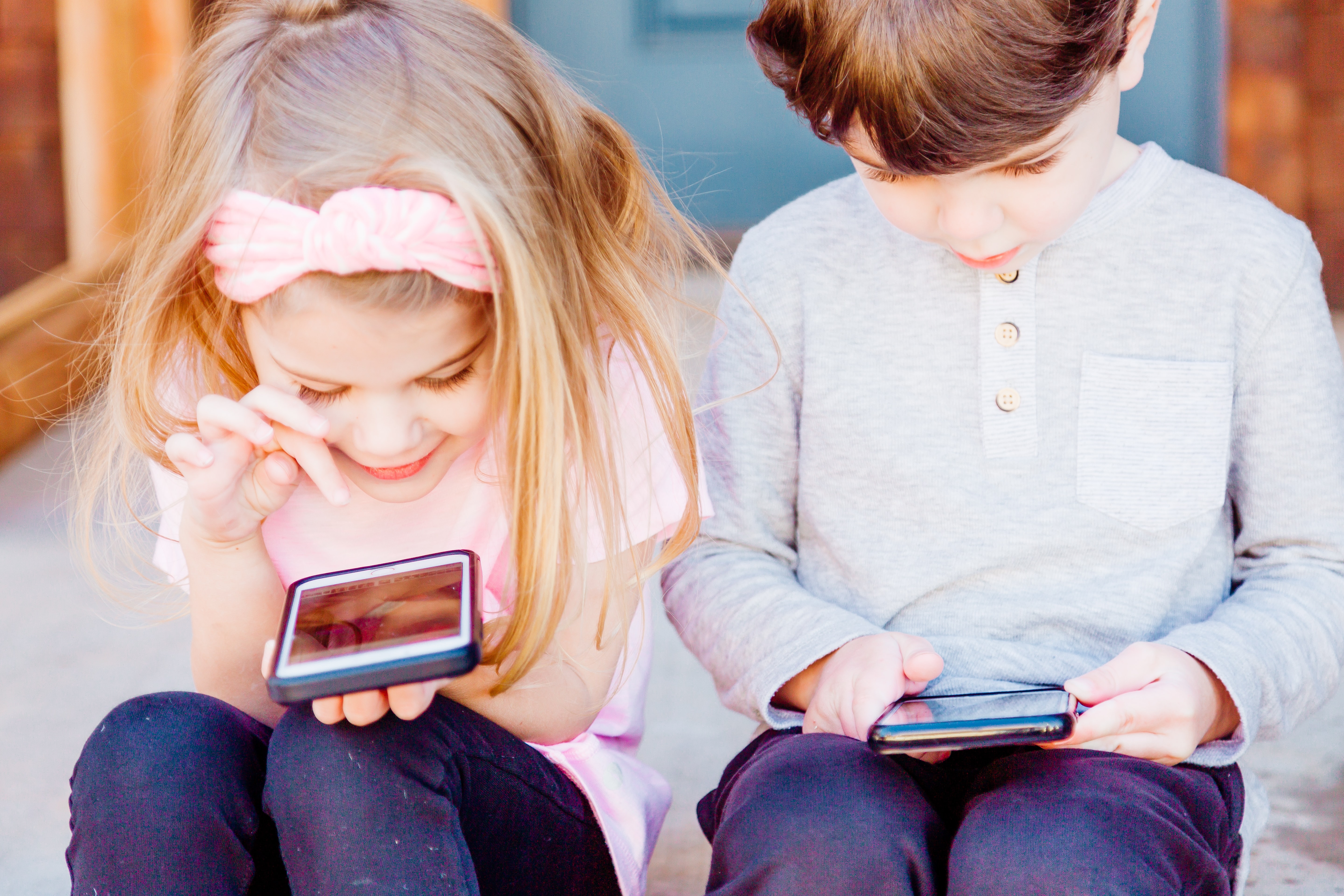 Two young kids look at cell phones.