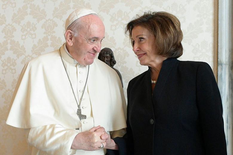 Pope Francis and Speaker Nancy Pelosi stand next to each other, making eye contact and holding hands.