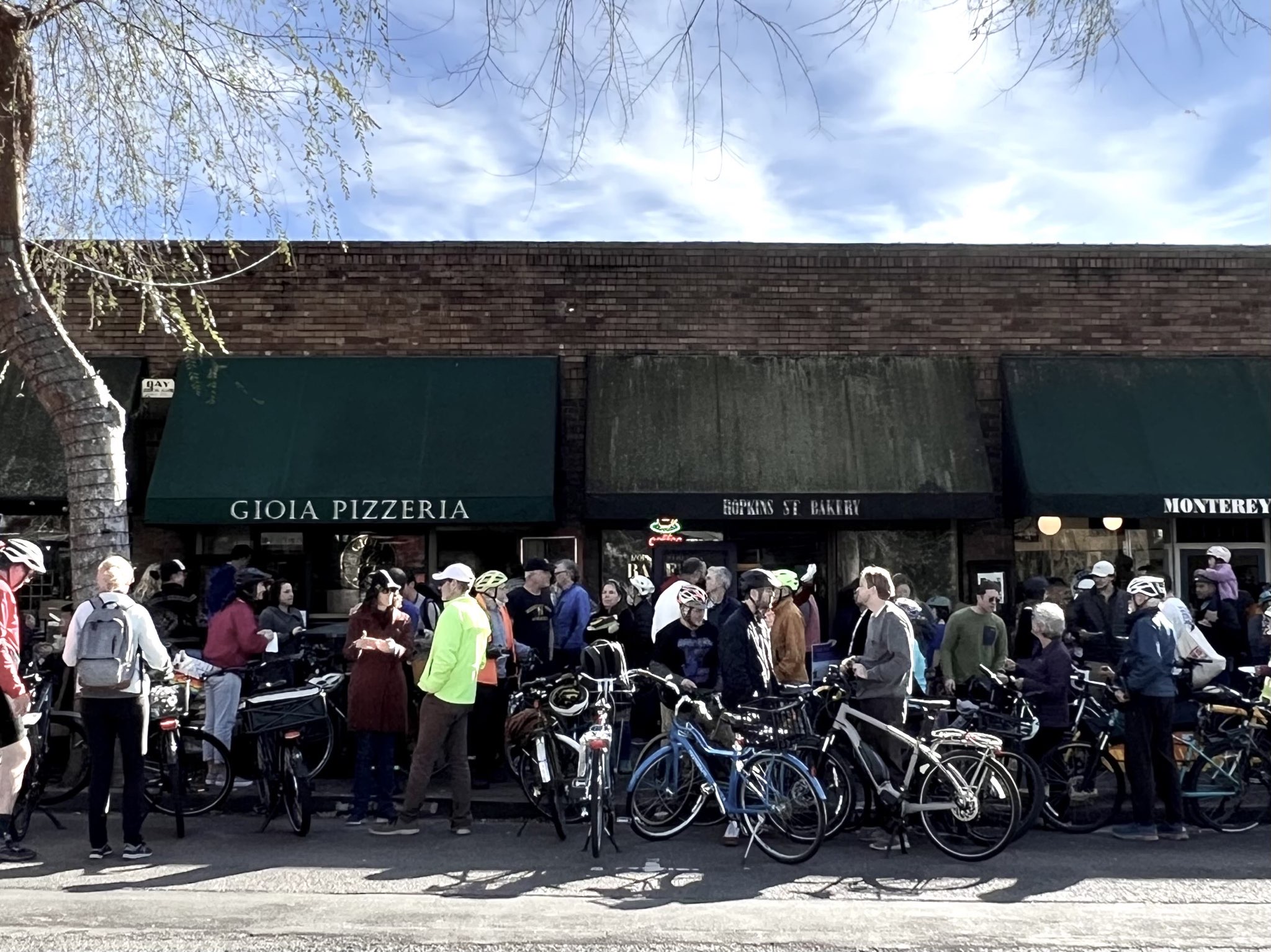 Photo of a multi-generational group of people, many with bicycles in front of Hopkins Street businesses