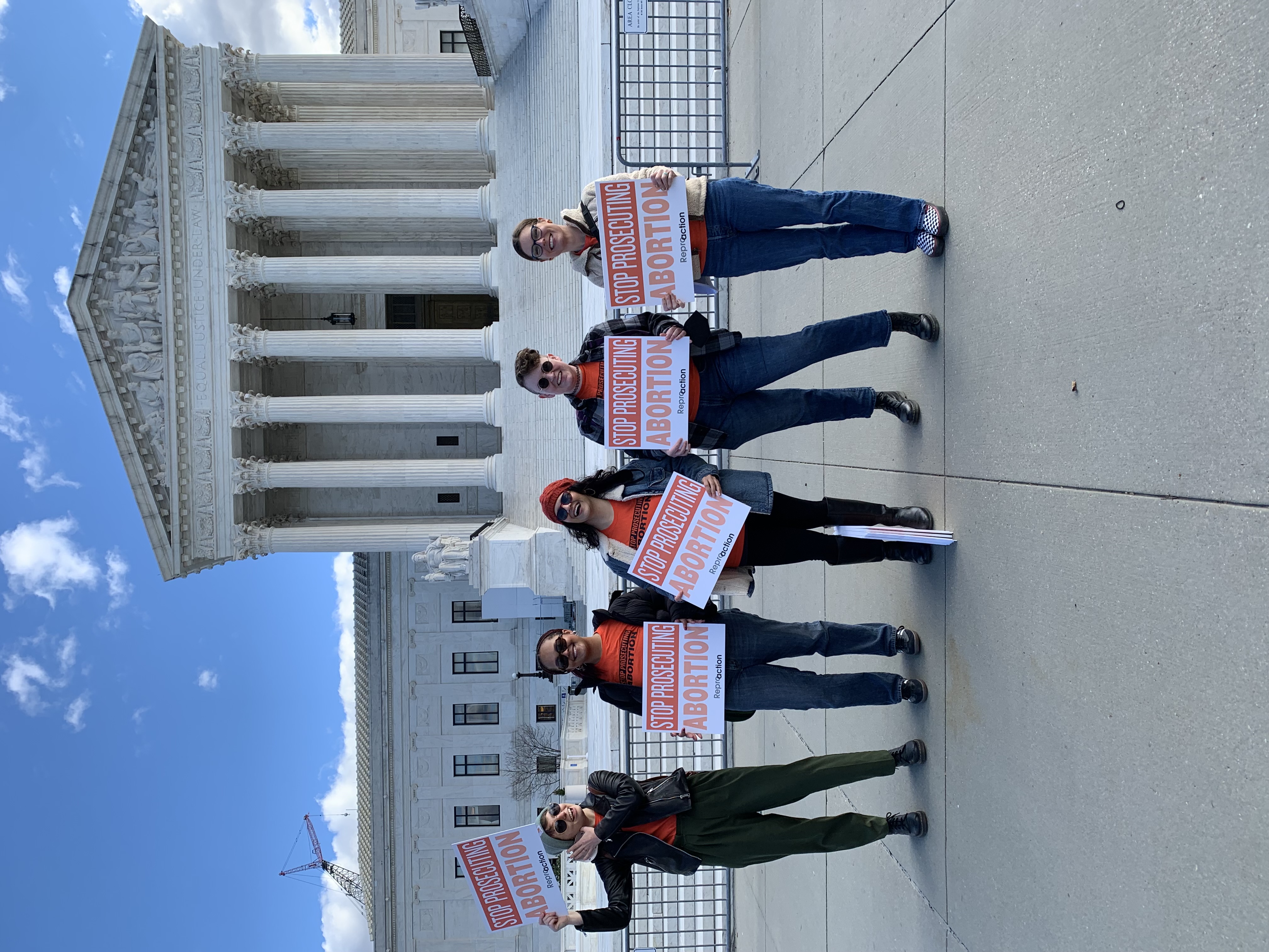 [alt text: 5 people holding signs reading “stop prosecuting abortion” standing outside the Supreme Court]