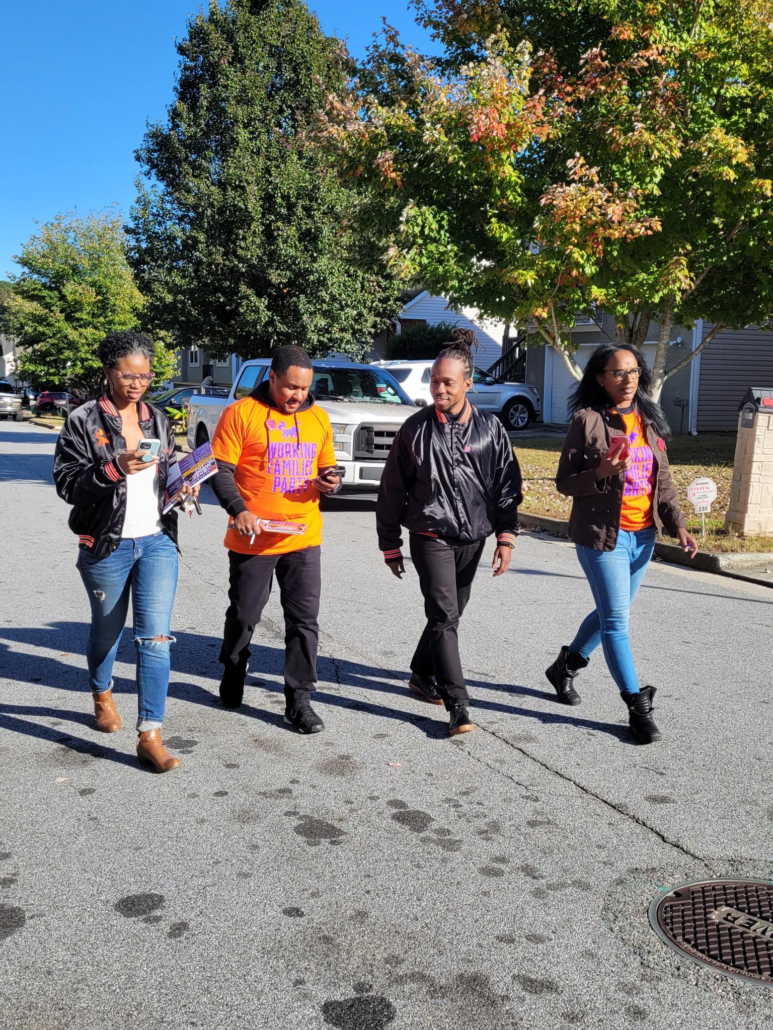 Four canvassers walking down the street on a sunny fall day. They are all wearing WFP swag and are smiling.