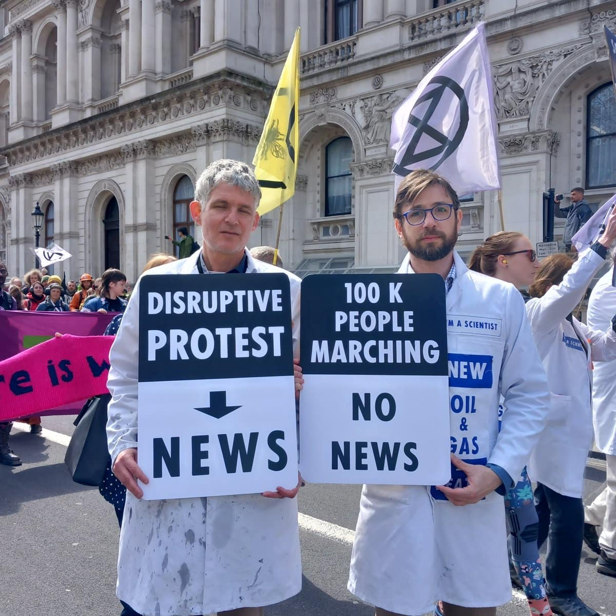 Rebel scientists hold signs saying 'disruptive protest = news' and '100k people marching = no news'
