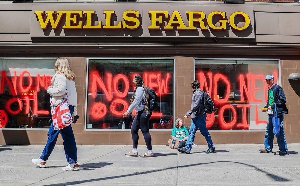 Commuters pass a Wells Fargo branch with 'no new oil' repeatly scrawled over its windows.