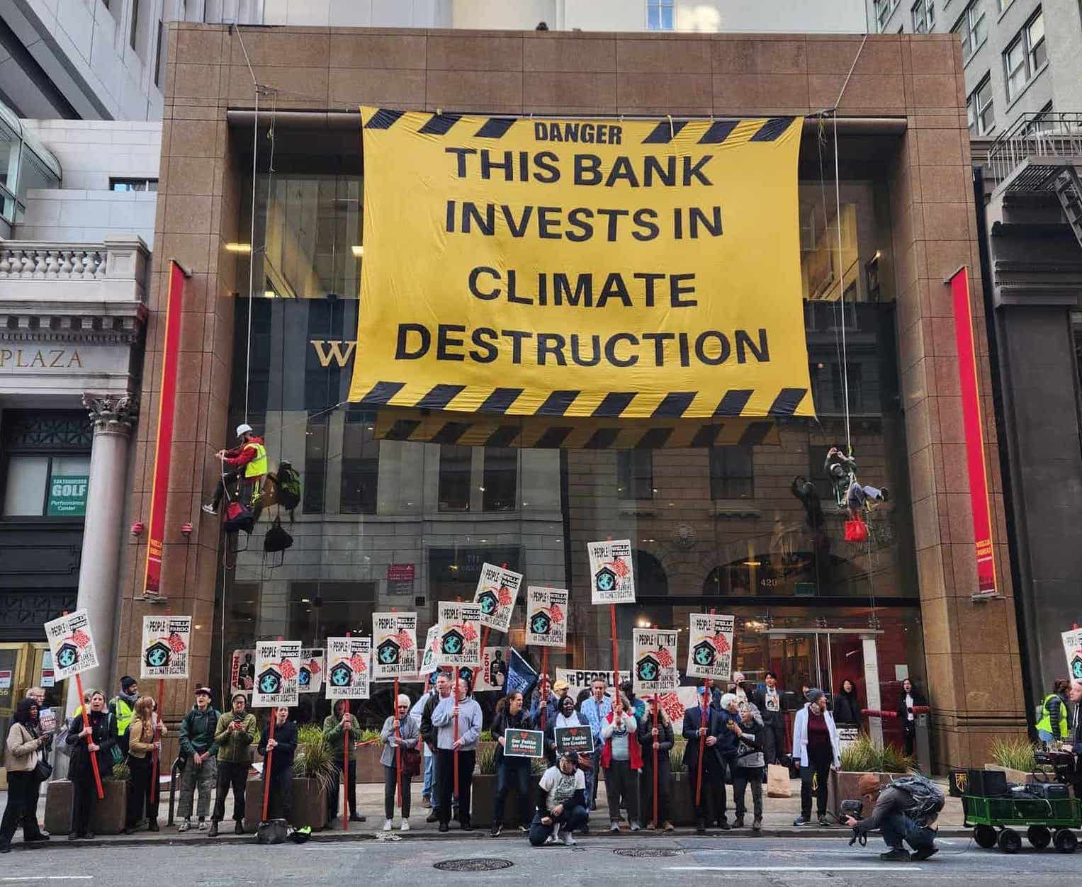 rebels stand outside a bank which is half covered with a banner saying 'this bank invests in climate destruction'