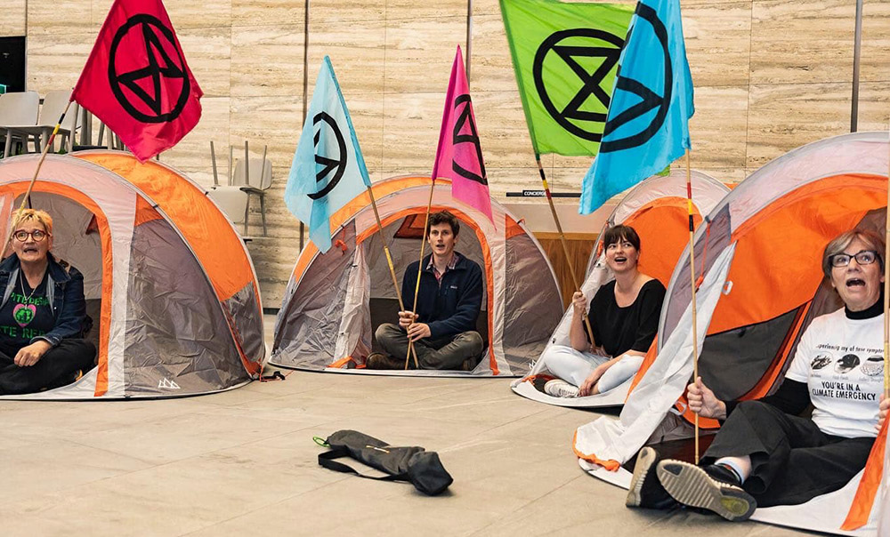 Rebels peer out from pop-up tents holding flags and singing in a marble foyer
