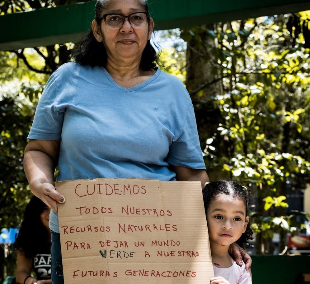 A mother and daughter stand together holding a sign.