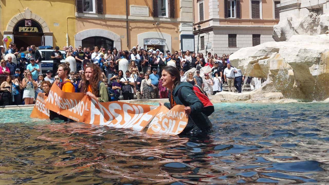 Protests wade in the fountain with a banner as tourists look on
