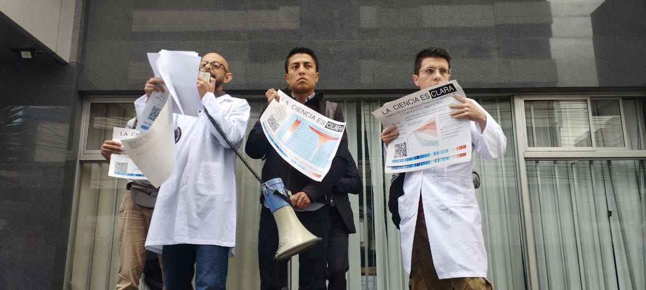 3 scientists hold scientific papers while one speaks on a megaphone