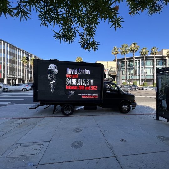 Photo of mobile billboard saying "David Zaslav was paid $498,915,318 between 2018 and 2022. We stand with actors and writers! Working Families Party" Photo of David Zaslav.