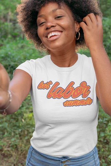 Black woman with afro and gold hoop earrings wearing a white shirt with orange letters that says hot labor summer 