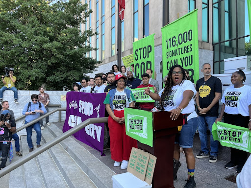 Photo of the Stop Cop City coalition with signs dropping off 116,000 signatures at city hall. 