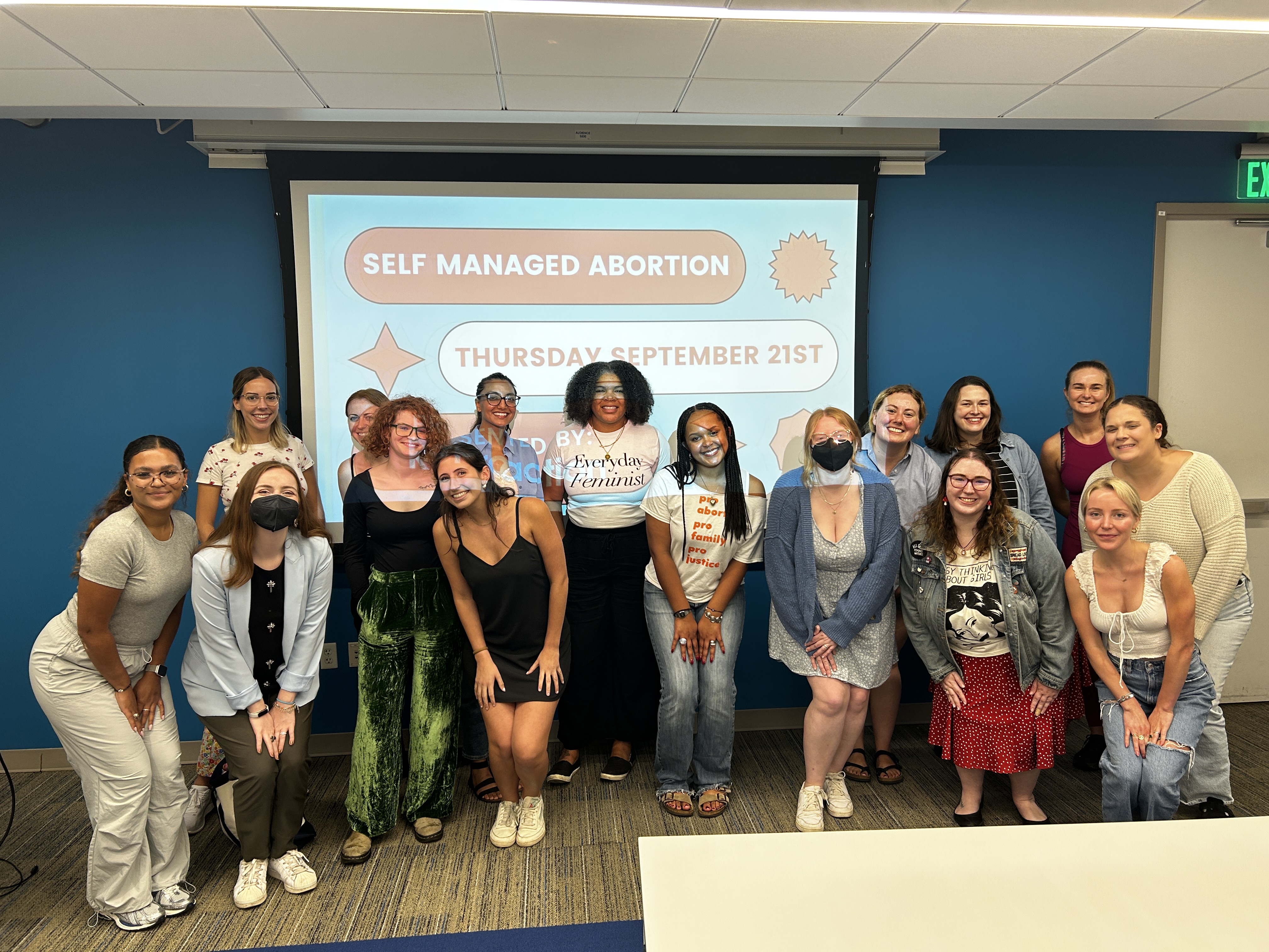 Picture of over a dozen people crouched in front of a projection screen in a classroom. Projection screen states: Self-Managed Abortion; Thursday, September 21st.