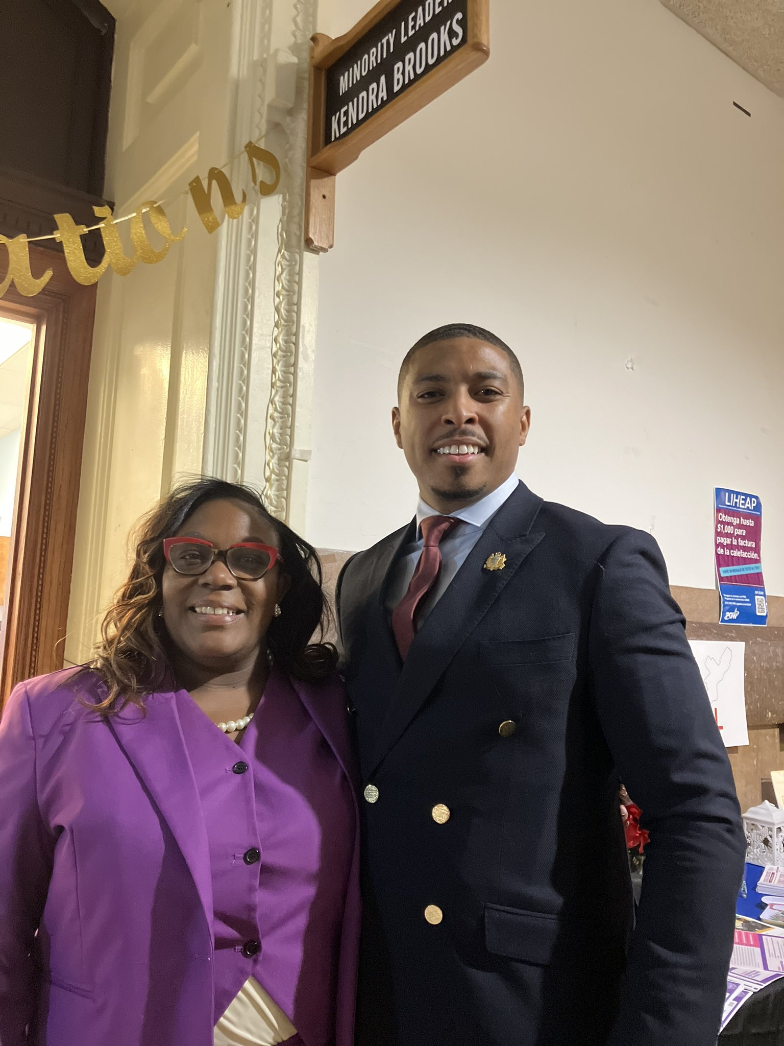 Councilmembers Kendra Brooks and Nicolas O'Rourke smile for the camera under a sign that reads Minority Leader Kendra Brooks