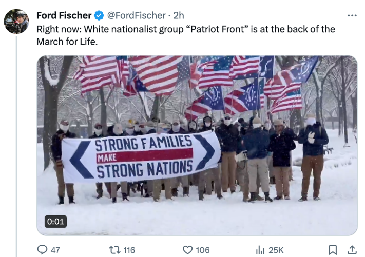 A screengrab of an X (formerly Twitter) post from Ford Fischer. Fisher’s text reads “Right Now: White nationalist group “Patriot Front” is at the back of the March for Life” The photo shows a group of men with face covers wearing blue jackets and khaki pants stands in the snow. A banner they hold reads: Strong Families make strong nations. They hold several flags that are red and white striped with a blue corner however one of the flags is upside down and in several the blue corner has a circular star design and other designs associated with the group Patriot Front. 