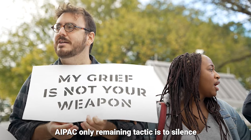 Screencap from Reject AIPAC ad showing two protestors with a sign saying 