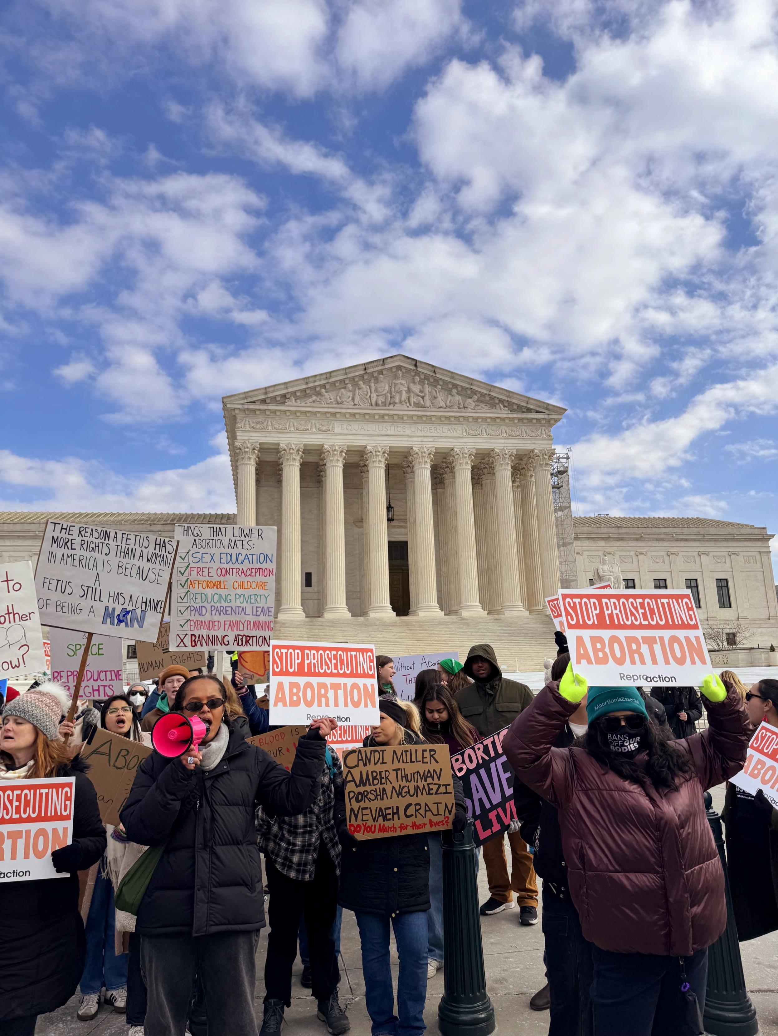  A group of people holding protest signs in front of the Supreme Court.