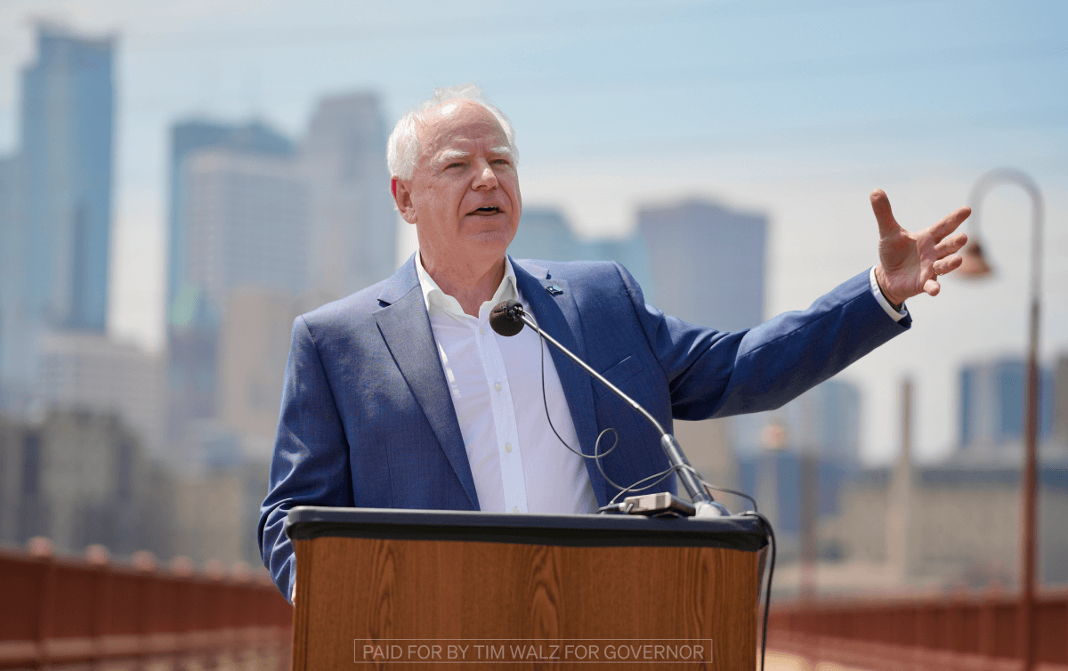 Tim Walz stands at a podium with a skyline in the background