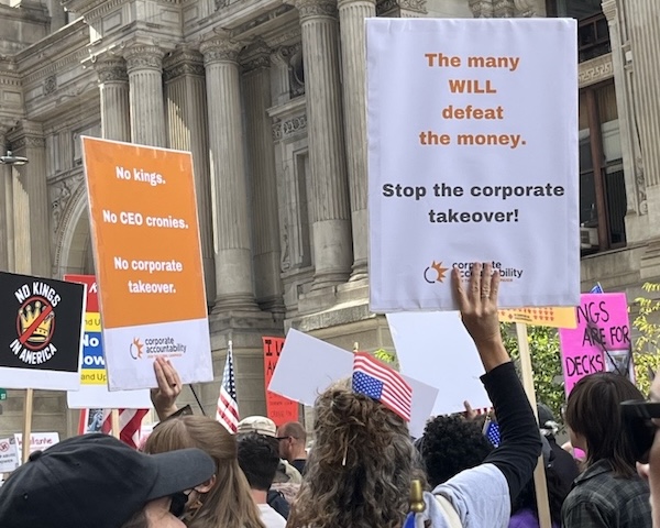 Activists at No Kings protests holding a sign that reads 'The many will defeat the money