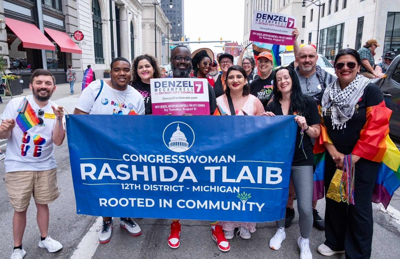Rashida marches in the pride parade with a banner, surrounded by LGBTQIA+ people.