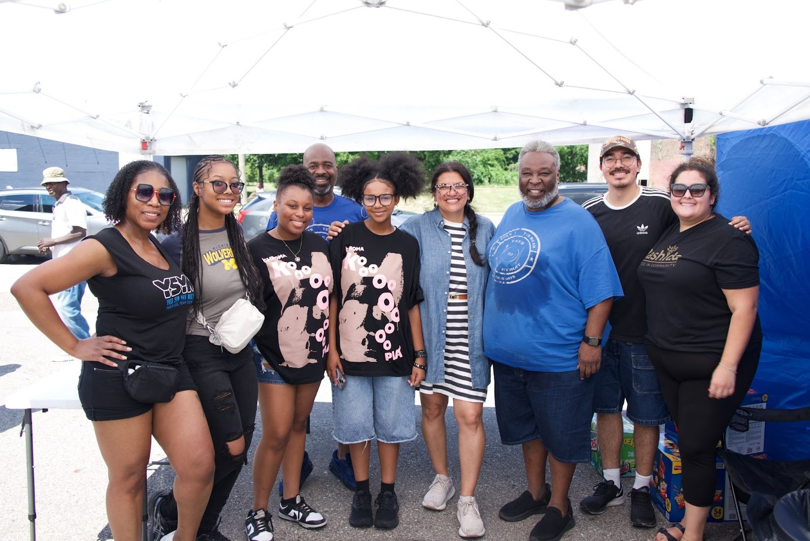 Rashida stands under a tent with volunteers after boxing up hot meals