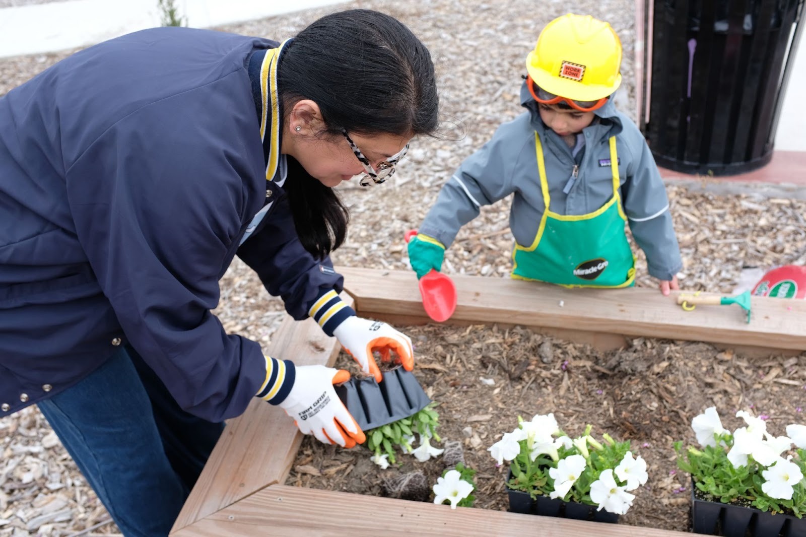 Rashida helps a child plant a flower in a flowerbed.