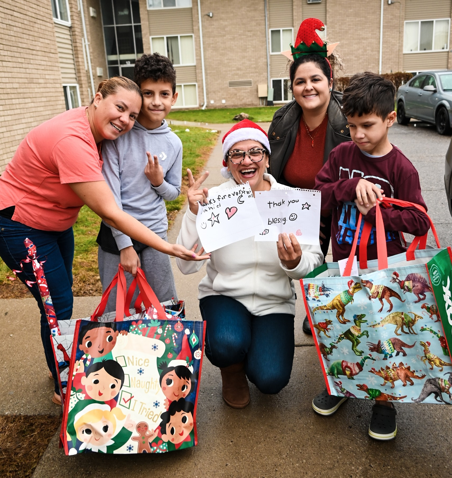 Rashida kneels next to two kids, holding cards saying thank you for the gift bag.
