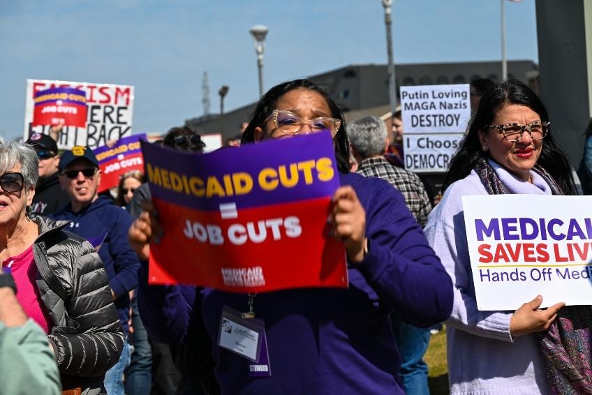 Rashida marches with healthcare workers holding a sign "Medicare saves lives"