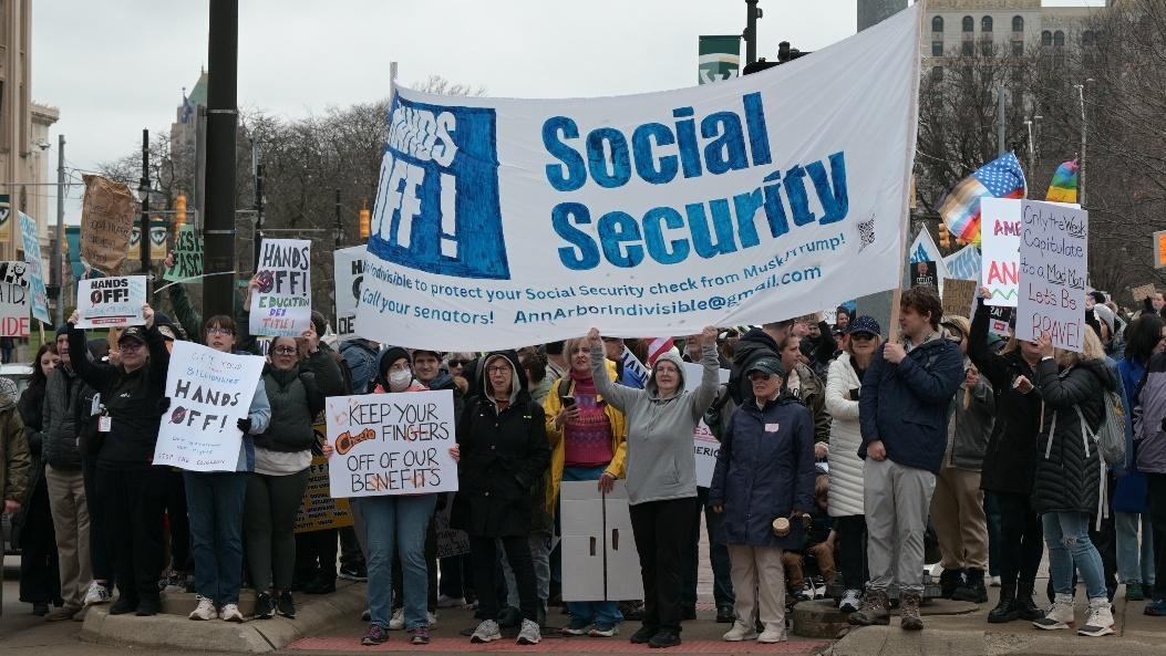 Rashida joins a rally with a large banner that says 'Hands Off Social Security'