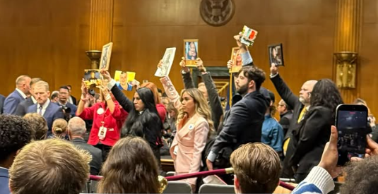 Families and activists raise one hand holding a photo of their loved one, detained by ICE