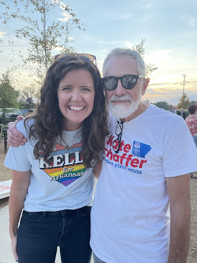 Photo of Kelly and a man standing outside and smiling at the camera. They are both wearing campaign t-shirts. Kelly is wearing a white Kelly for Arkansas shirt, and the man is wearing a Kate Schaffer for Arkansas State House. He is also wearing black sunglasses.